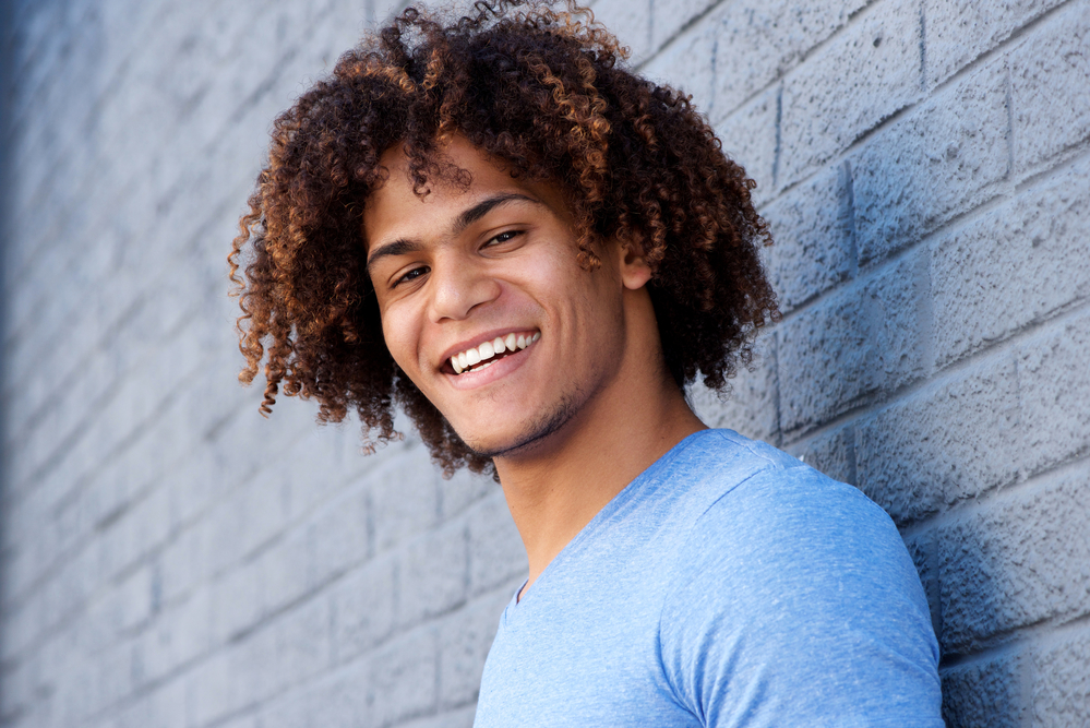 The young man's hair is styled in loose waves, enhancing his thick, long locks, styled in a trendy dark brown to tan ombre.