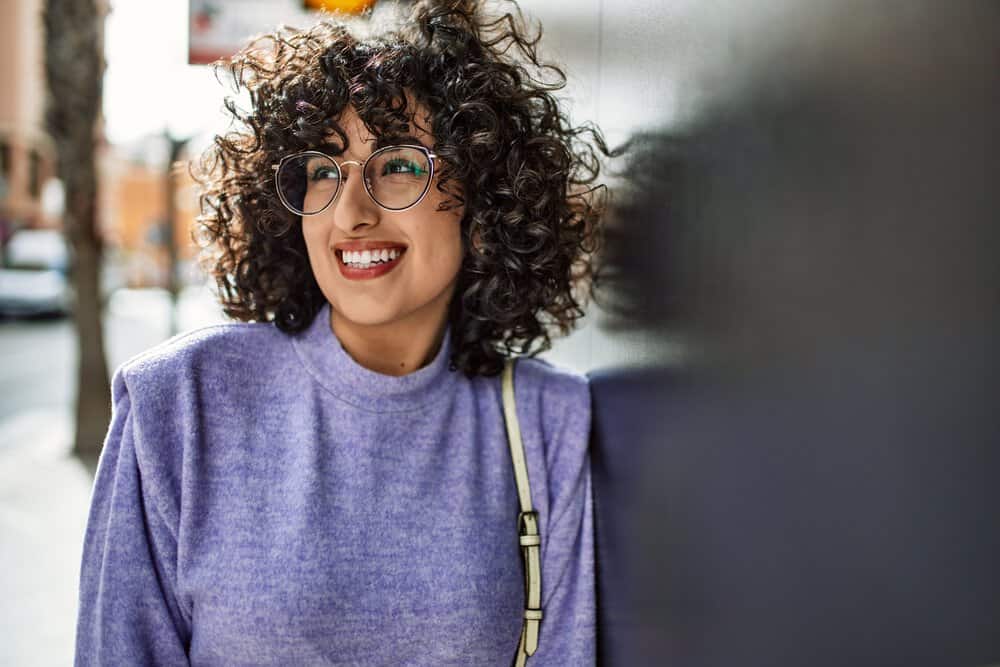 A gorgeous young female with light-brown skin showcases her hair growth, uneven distribution of hair follicles, and curl pattern, styled with a curling iron for stunning curls.