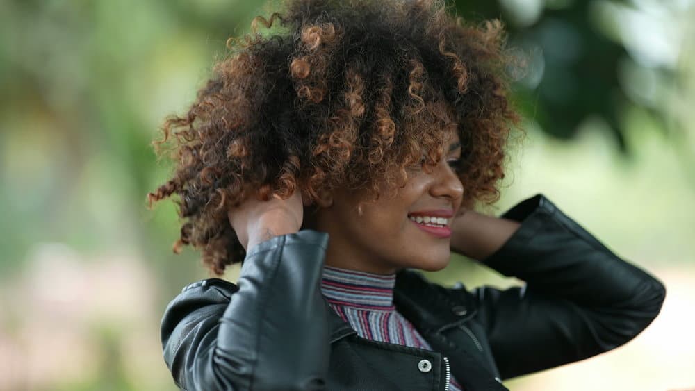 A stunning black female with light brown hair mixed with rose gold dyed hair strands showcases her warm skin undertones and hair texture, styled to highlight her face shape.