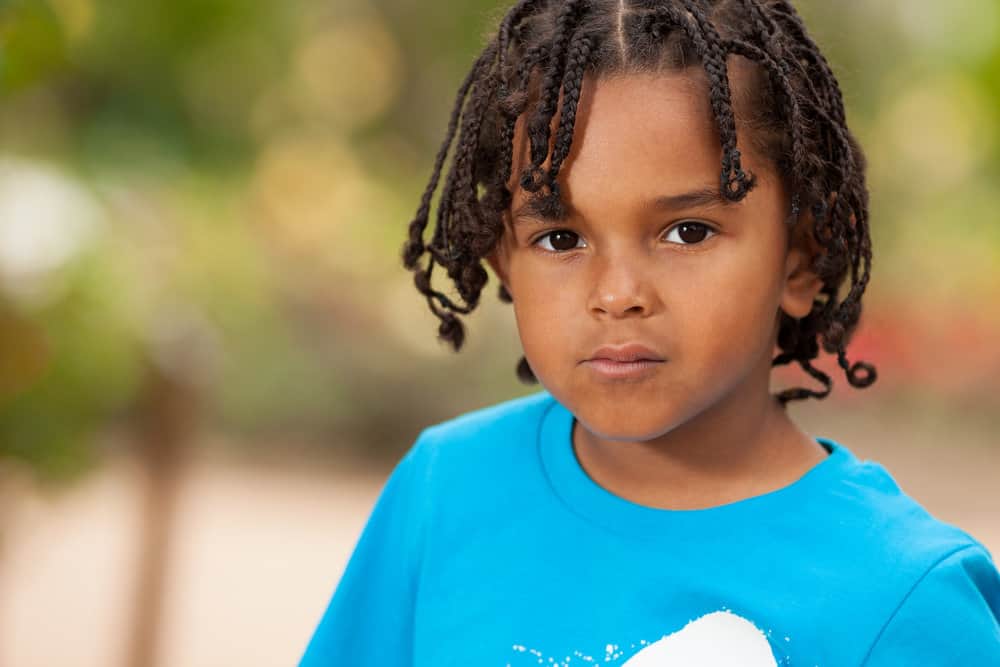 The cute African American toddler rocks long, tiny braids on his type 4 natural hair, showcasing a stylish and age-appropriate braided hairstyle.