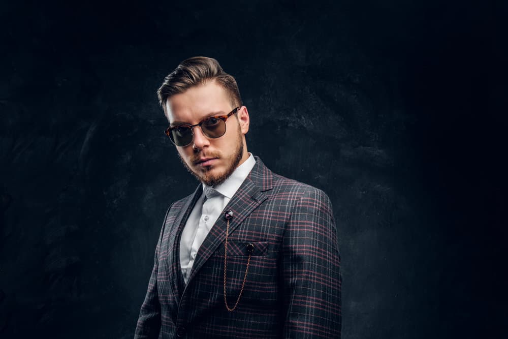 A young white man wearing a John Shelby haircut with a disconnected undercut from Peaky Blinders and a lumberjack-style beard.