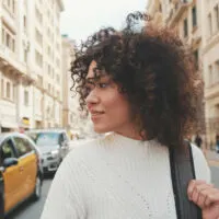 A young female woman with natural curls plans to follow a hair care regimen based on the curly girl method after using a gentle clarifying shampoo to clean her hair.