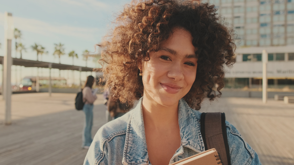 A beautiful young black girl wearing dark brown heat-free hair with natural curls enhanced by using curly hair extension wefts made from Remy human hair.