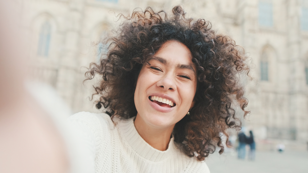 A beautiful young black woman with curly thick hair that was styled with a Dyson Supersonic hair dryer with a gentle air attachment and frizz-free hair tools.