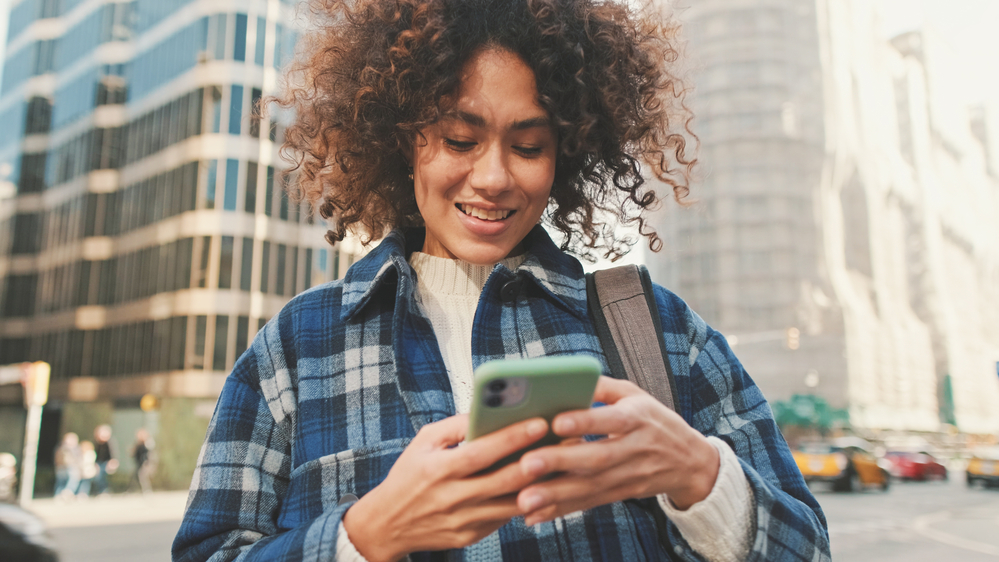 A beautiful black female is using to mobile phone to research whether halo hair extensions and fusion hair extensions can be worn on fine or thin hair stands.