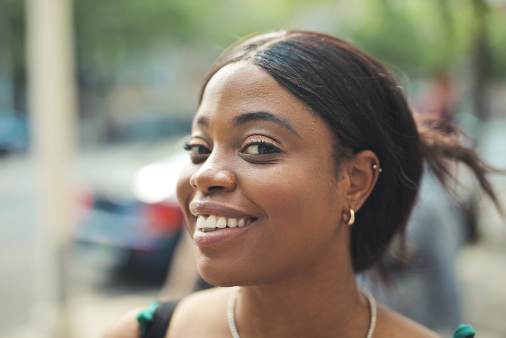A young woman with a great smile wearing a lace closure wig with a natural hairline and a slightly wavy, thicker hair texture complimenting her dark brown skin tone.