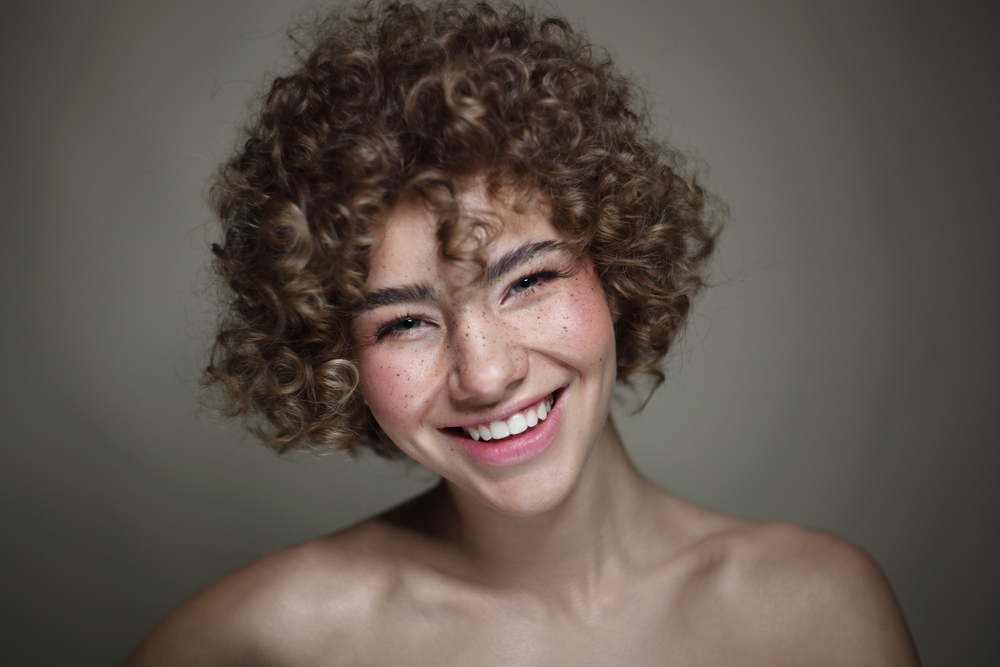 Her wavy hair shines through as she wears blunt bangs, perfectly blending with her voluminous curls for a stunning look that looks great on most curly haired girls.