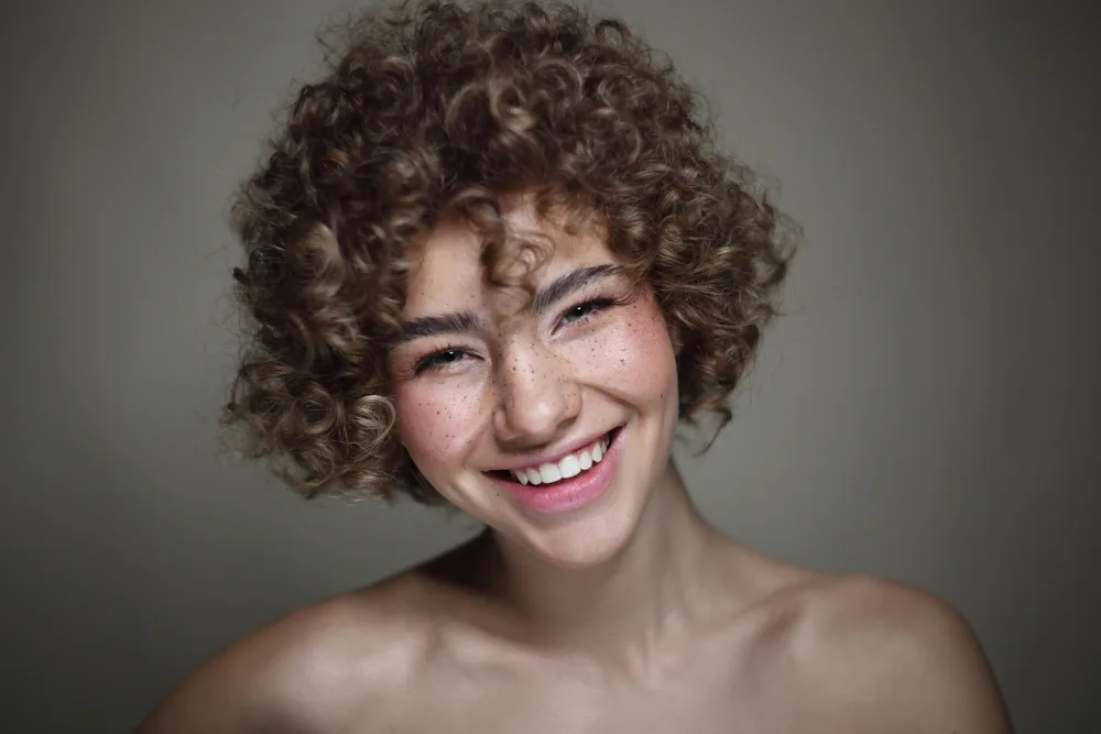 Curly Hair with Bangs: Curly Hairstyles with Fringe or Bangs 13 Her wavy hair shines through as she wears blunt bangs, perfectly blending with her voluminous curls for a stunning look that looks great on most curly haired girls.