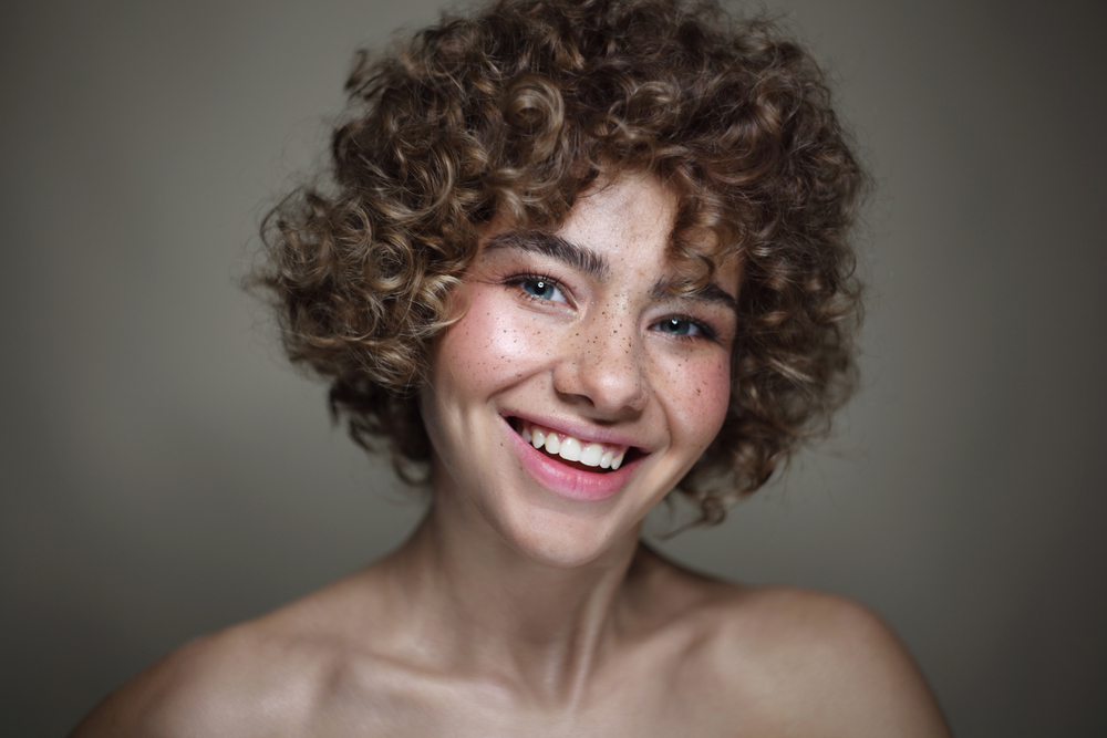 Embracing her voluminous curls, this girl with short curly hair wears blunt bangs that perfectly frame her face, adding a touch of playfulness to her curly hairstyle.