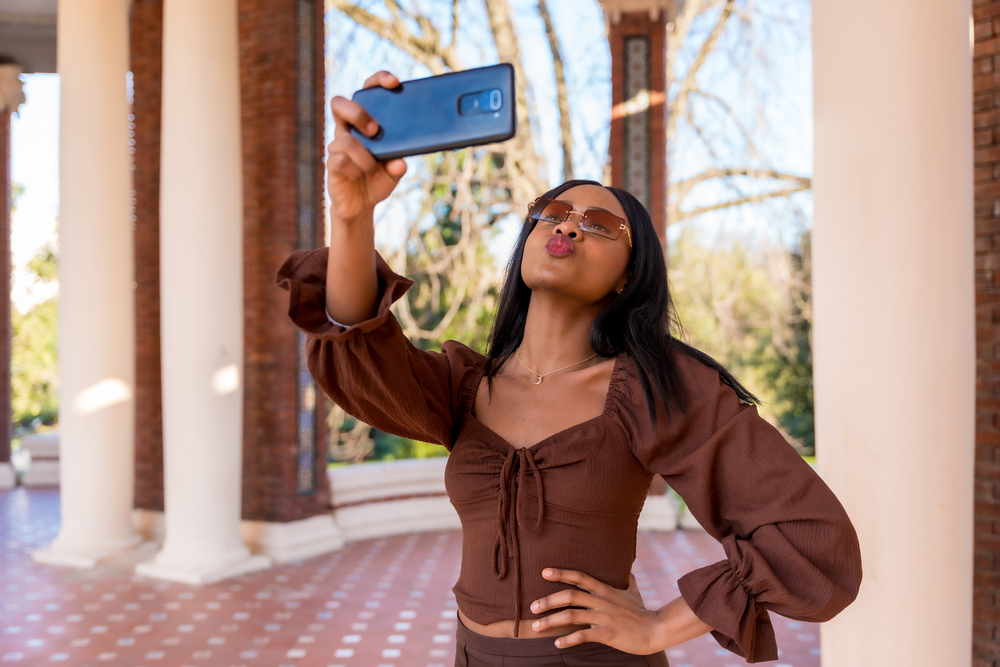 A beautiful black girl takes a selfie after using bleach on wet hair to dye her natural hair a light brown color.