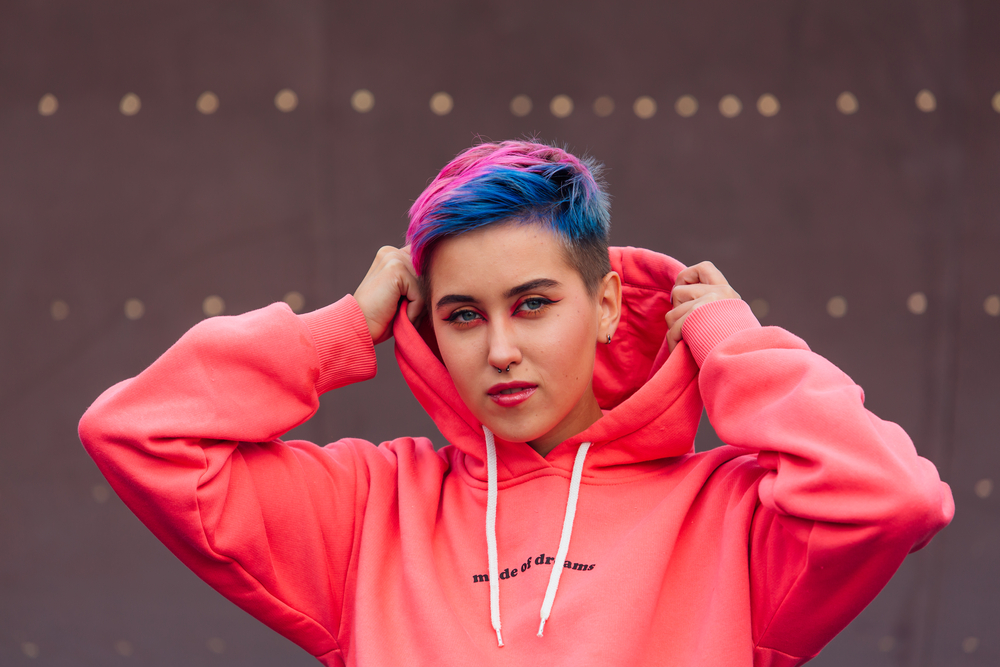 A cute young girl with colorful short hair is wearing a gender neutral haircut that looks like an androgynous look that Miley Cyrus would wear.