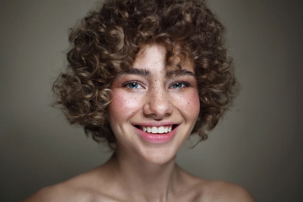 With wavy curtain bangs that beautifully frame her face, this girl's curly hair adds an extra layer of style and elegance.