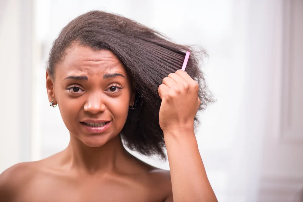 Fixing Tangled and Severely Matted Hair After Hospital Stay 1 A disappointed black female with matted hair strands is combing through her hair with a wide-toothed comb after using detangling spray on lightly dampened hair.