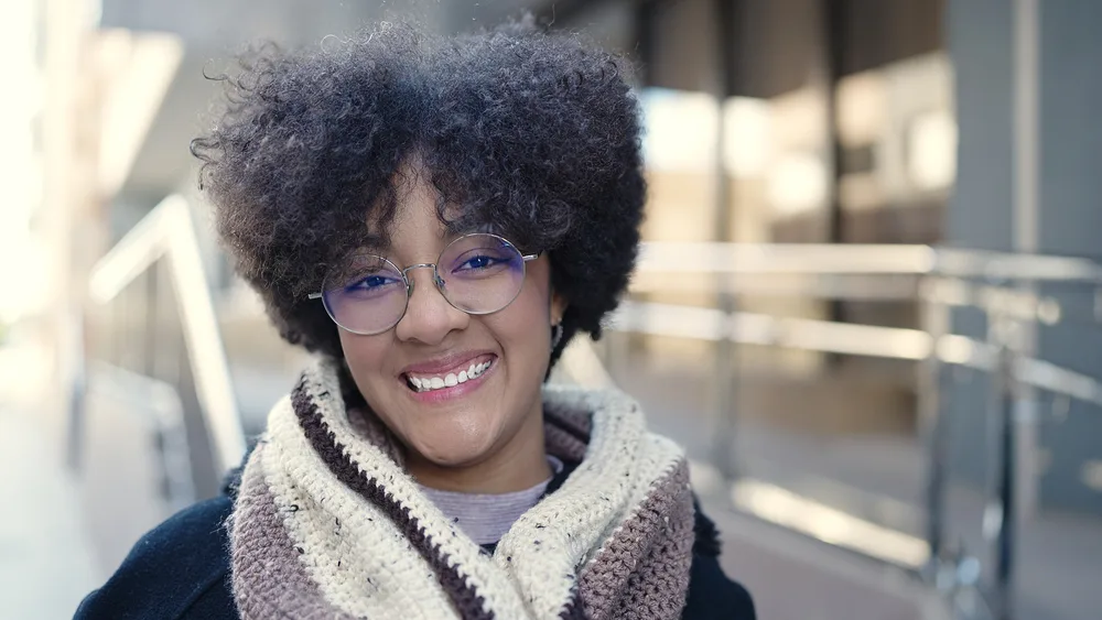 This young black woman embraces her looser hair texture with a beautifully styled curly hairdo, enhanced by the nourishing properties of whipped shea butter.