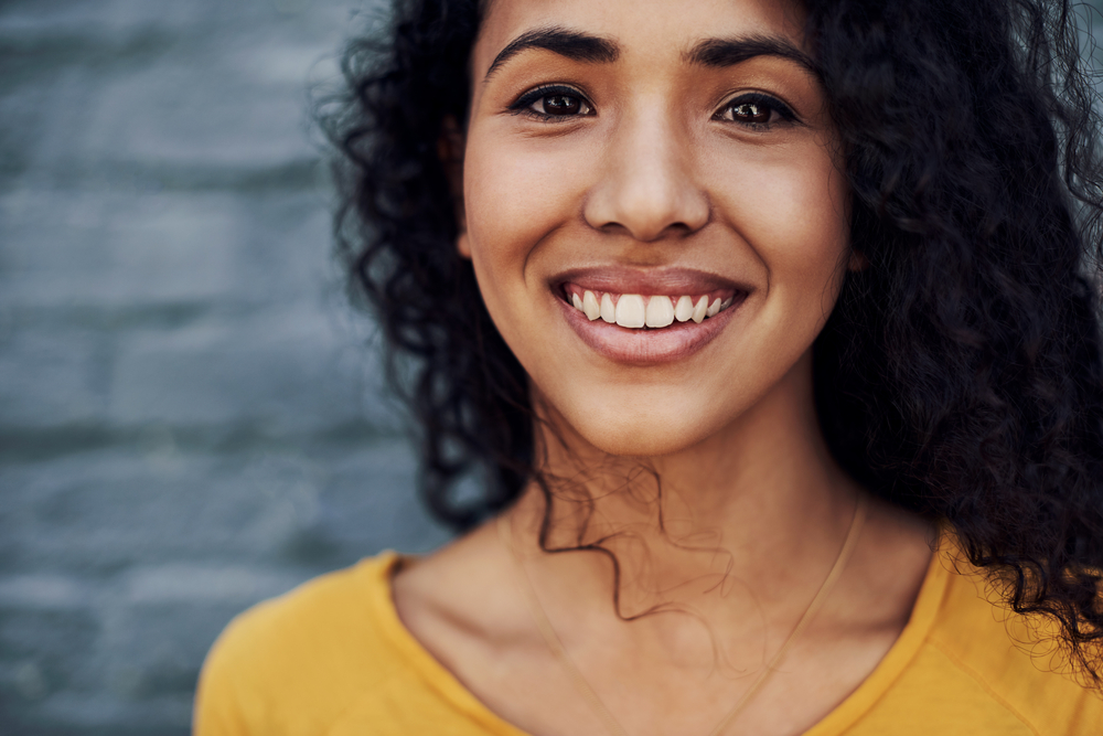 An attractive young woman standing outside after drying her soaking wet hair with a hair dryer and styling her low porosity hair strands with hair gel and shea butter.