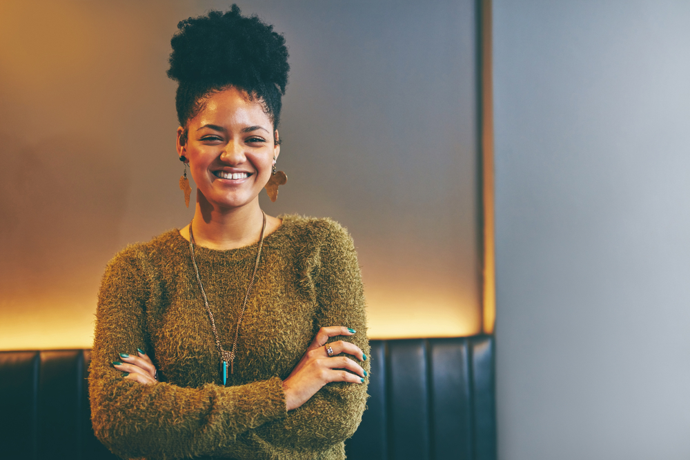 An attractive young woman with thick hair used coconut and moisture to wet hair before putting it into a pineapple style with thickening mousse that highlights her natural hair texture.