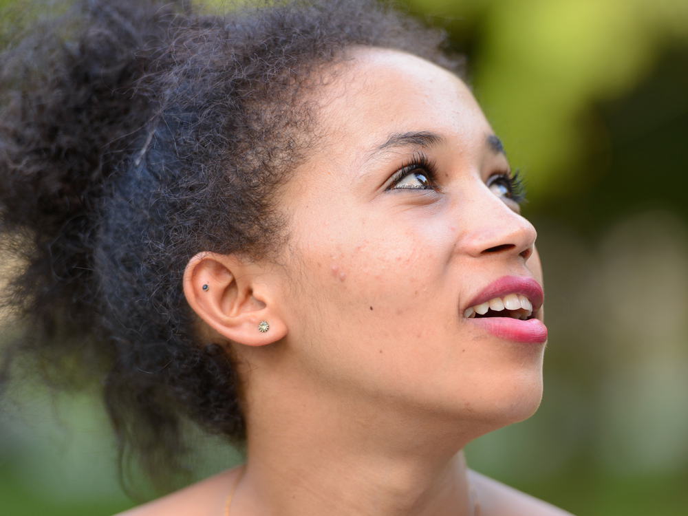 A young black female wearing an updo on type 3 hair strands secured by banana clips and bobby pins highlight the beautiful fine hair texture of kinky hair.