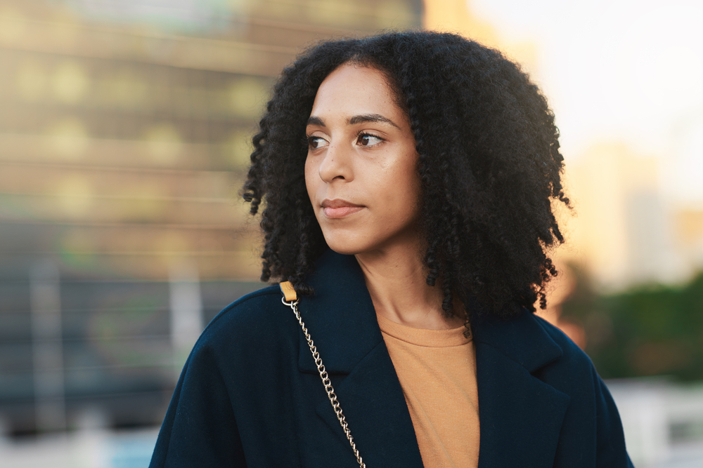 This black woman confidently flaunts her dry hair strands, showcasing the visible curl pattern and embracing her unique textured hair.