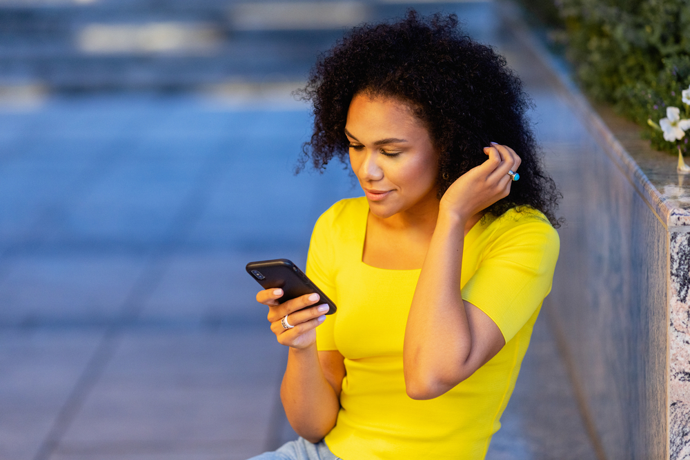 A beautiful female that's researching hair types on her mobile phone to determine which finishing spray is recommended for wet hair.