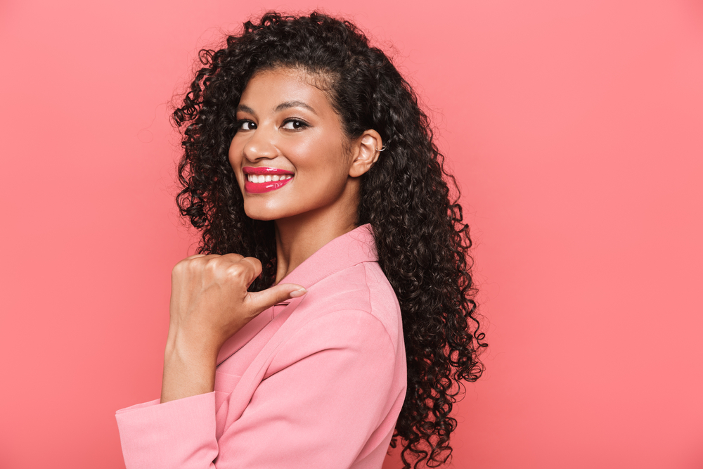 A lady wearing a pink business suit with beautiful armpit length curls.