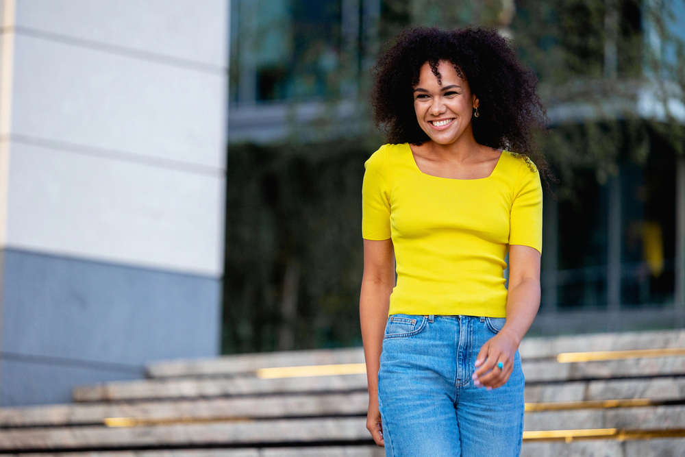 A black women with a beautiful smile took down her textured ponytail to reveal her natural texture, instantly achieving effortlessly chic waves.