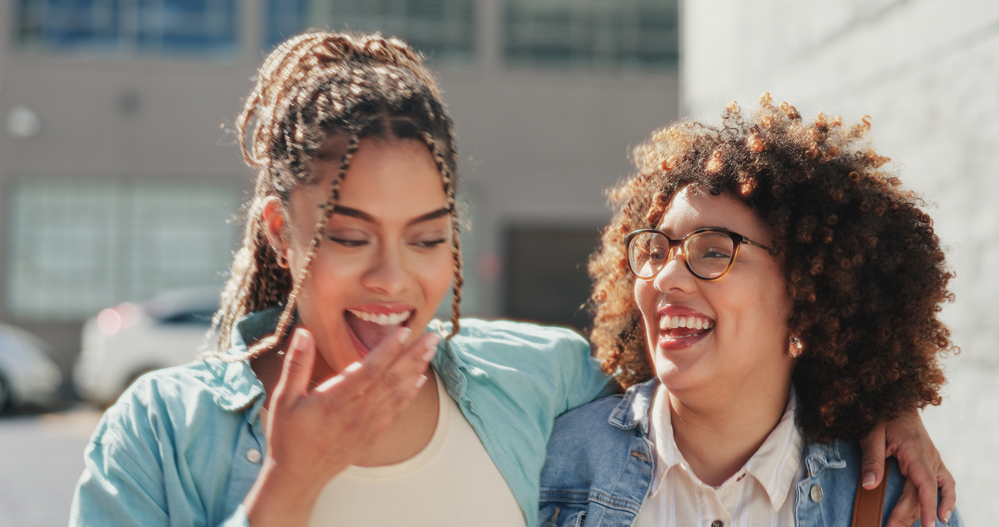 Two black girls wearing different curly hairstyles - one with black and blonde braids and the other with curly, frizzy hair strands.