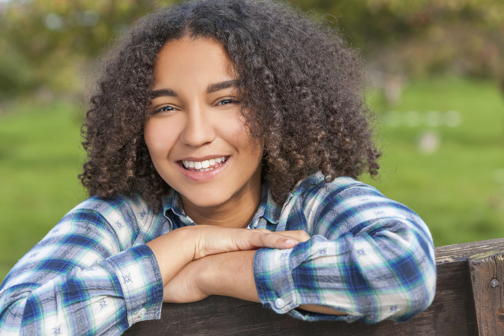 A female with shoulder length curl wearing a blue and white flannel shirt.