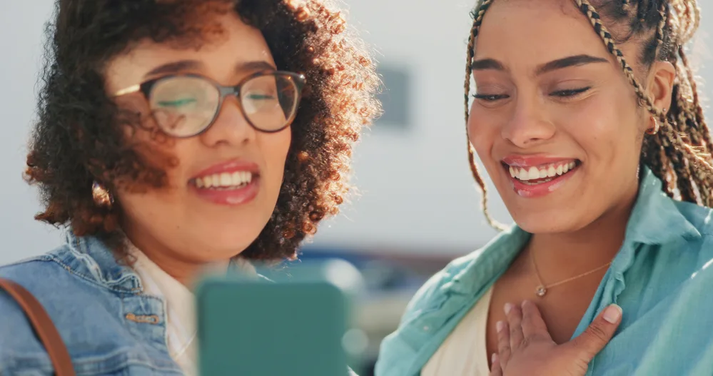 Castor Oil vs. Argan Oil for Hair: A Close Look at Both Oils 5 Two black girls with naturally curly hair strands researching whether argan targets dryness on an iPhone.
