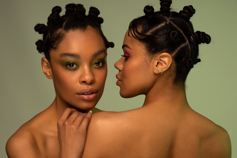 Two black ladies are wearing a Bantu knots natural hairstyle after using the praying hands technique to create larger knots.
