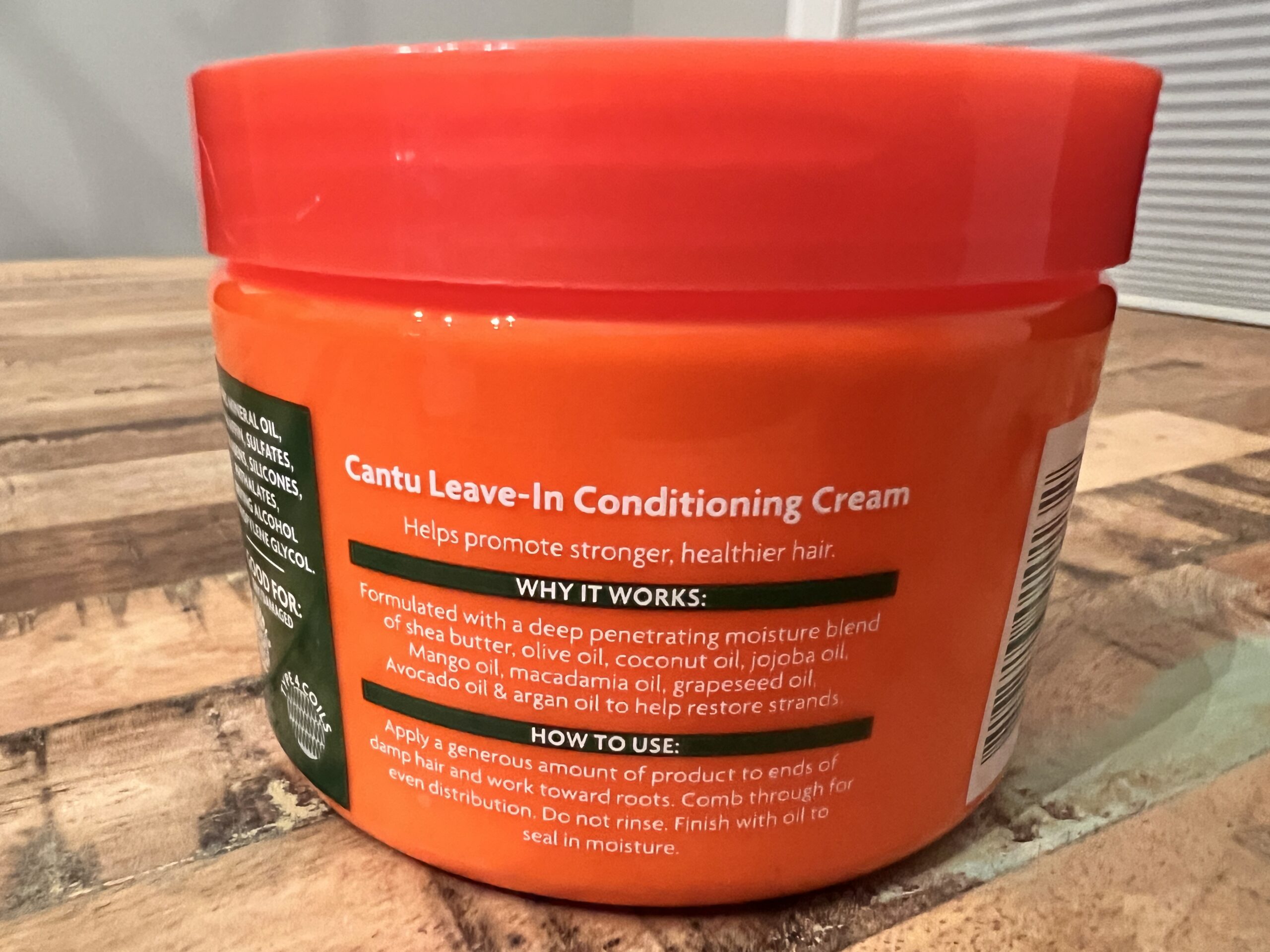 Hands applying Cantu Shea Butter Leave-In Conditioning Cream to hair, showcasing its use for repairing and softening hair.