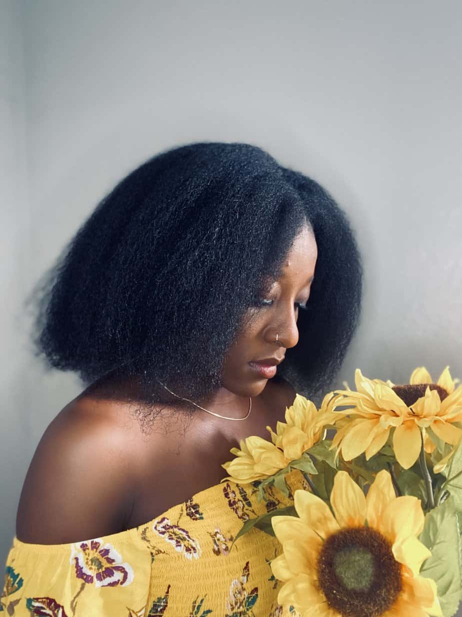 A woman with stretched 4C hair falling to just below her shoulders, holding sunflowers.
