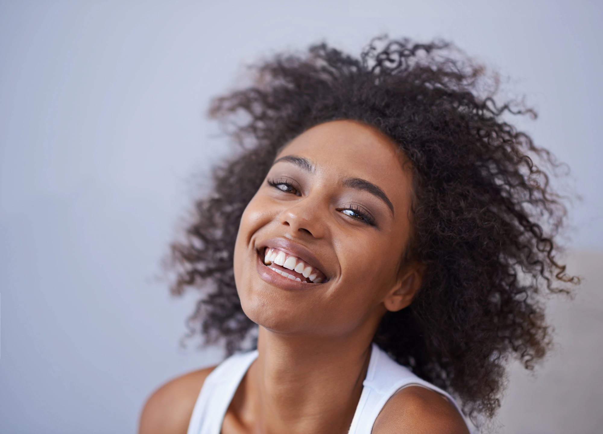 Shedding vs Breakage: How to Tell the Difference 1 A woman with a full head of tightly curled natural hair smiling, her curls loose and unstretched