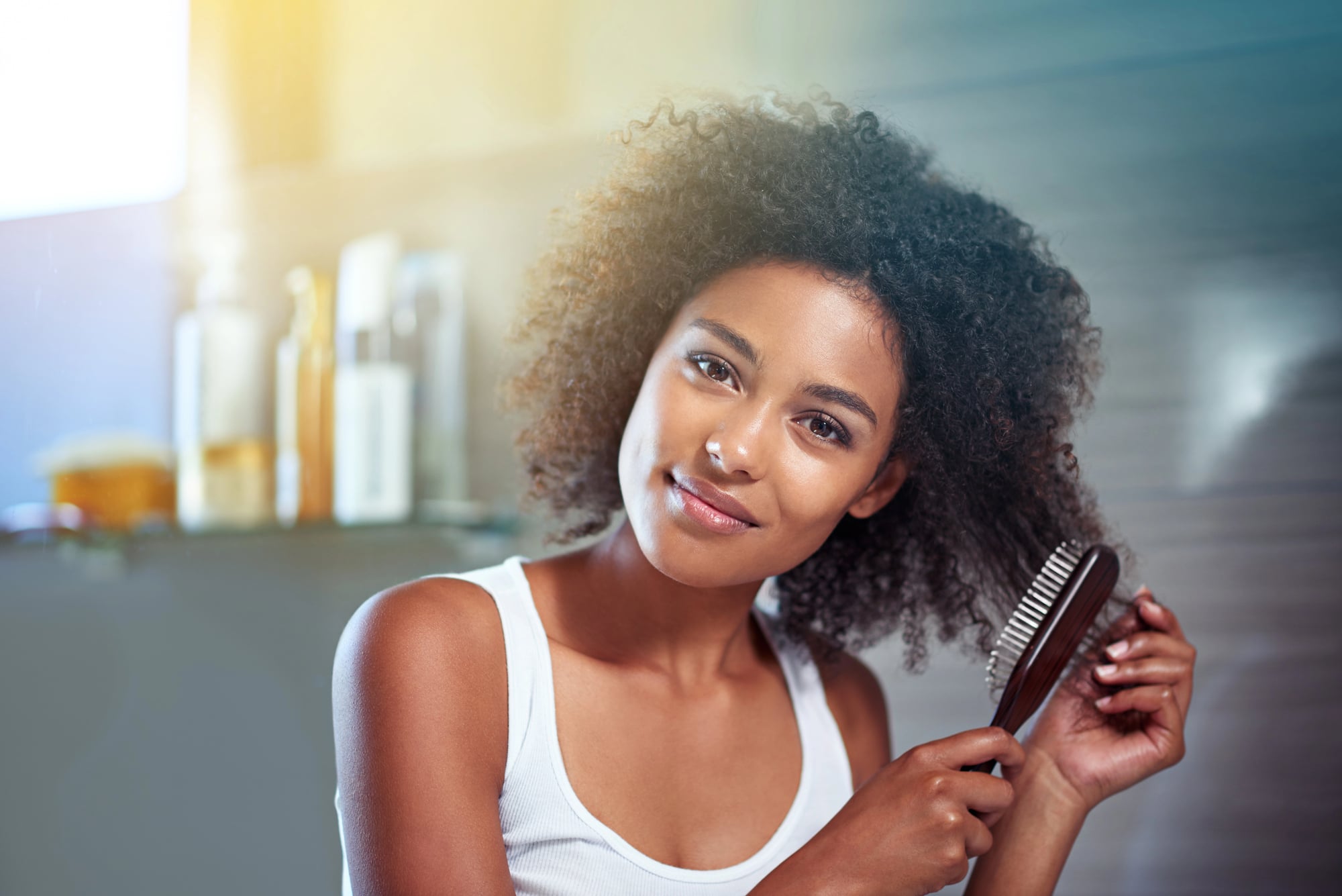 Shedding vs Breakage: How to Tell the Difference 4 The same woman working a wooden paddle brush through her curls in the bathroom