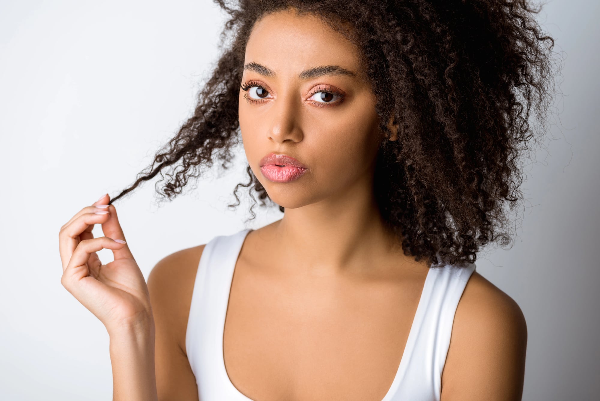A young Black woman with type 3 curls holding a single strand of her hair out from her face to show its length