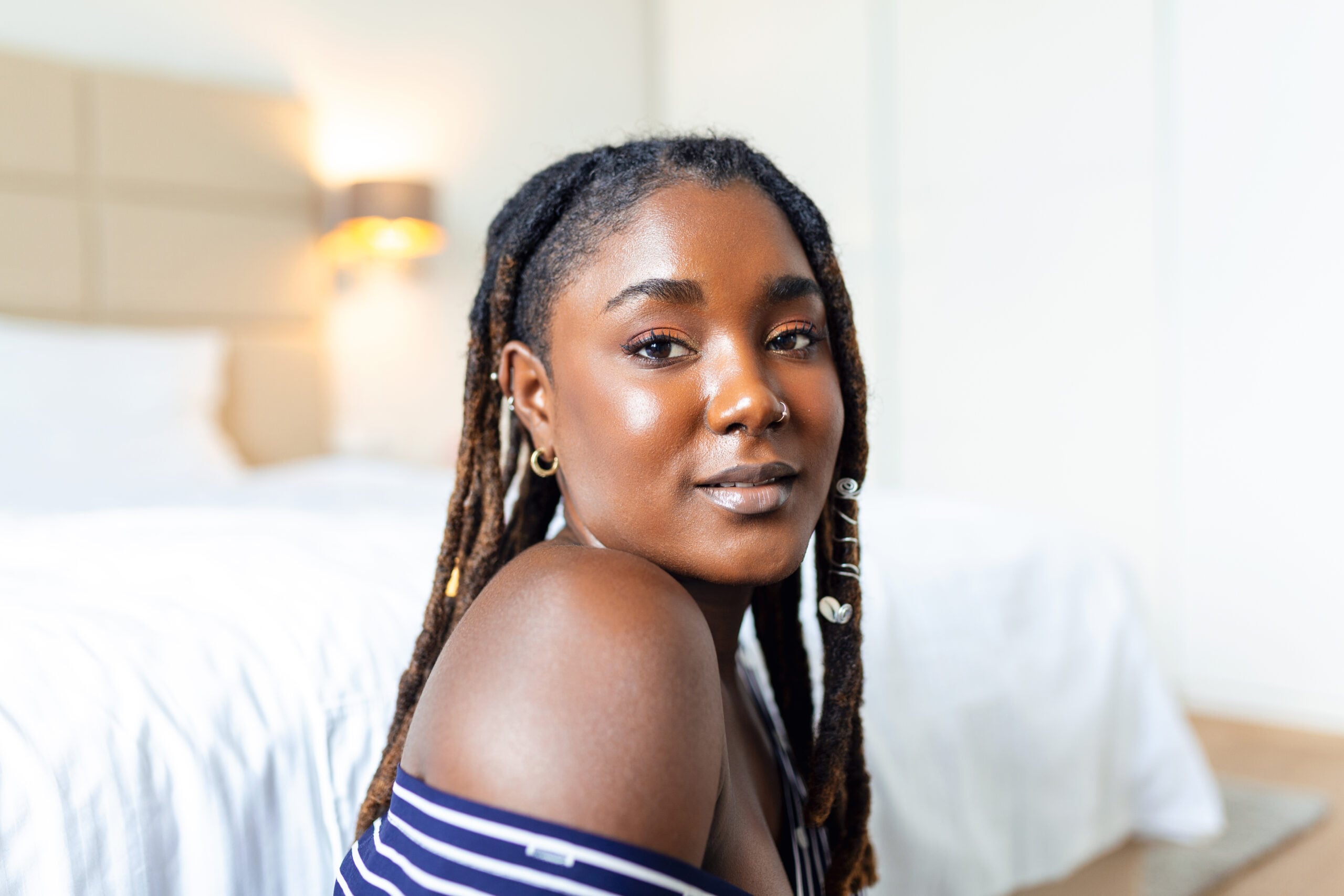 A Black woman with shoulder-length locs and silver loc cuffs, looking back over her bare shoulder