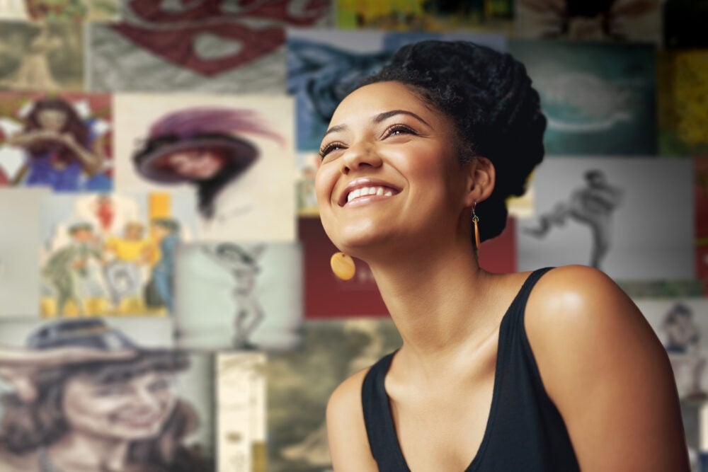 Black woman with a twisted updo smiling in front of a wall of artwork