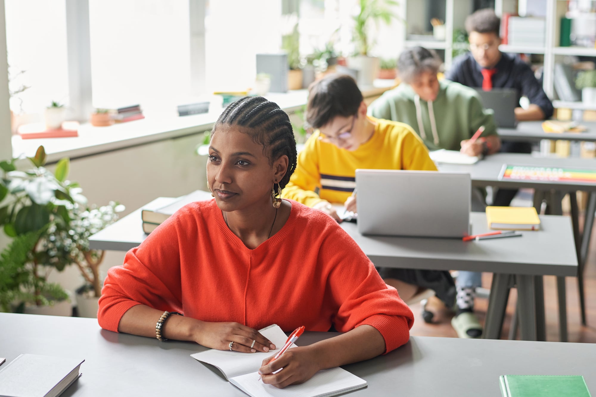 Black woman with cornrows writing in a notebook at a classroom desk