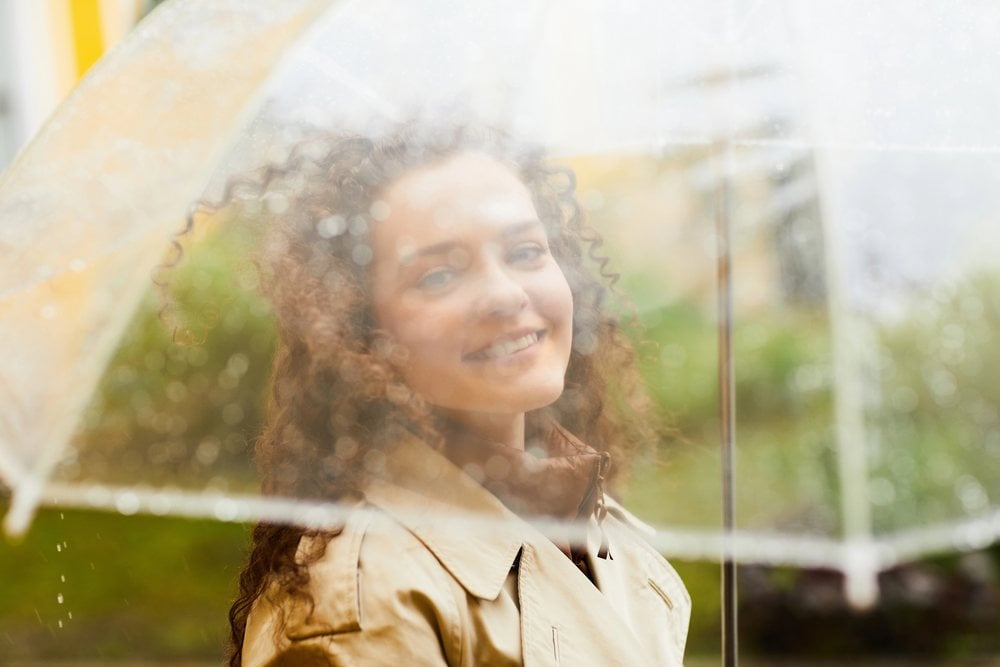 The same woman smiling through a clear umbrella covered in raindrops