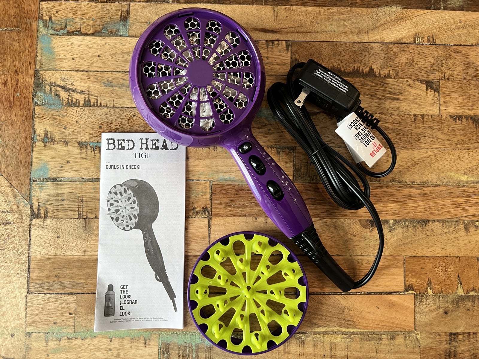 Purple Bed Head hair dryer with a diffuser attached, a second lime green diffuser, and its booklet on a wood table