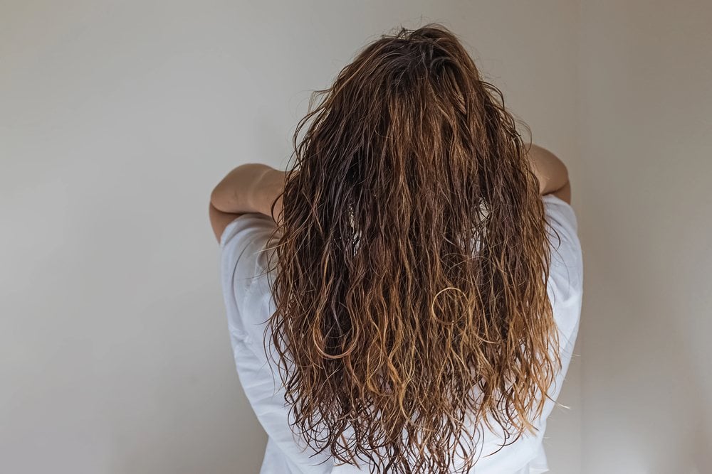 Back view of the same woman with long, light brown wavy hair spread over her white shirt