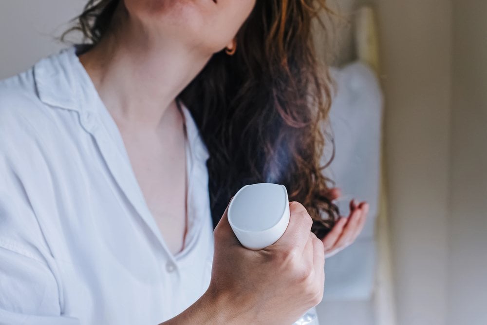Woman misting her damp wavy hair with a white spray bottle