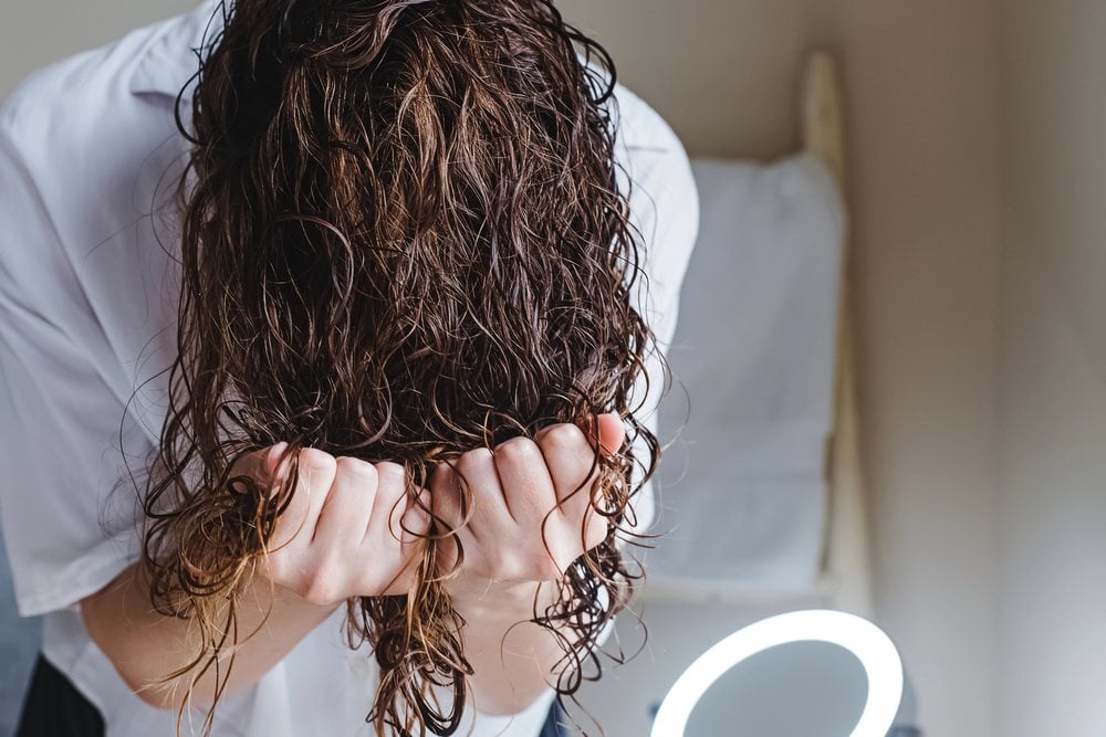 The same woman bent forward, scrunching her damp waves up toward her scalp with both hands